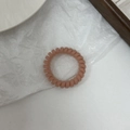 Matte bean paste color spiral telephone wire hair tie on a minimalist textured background - Orange