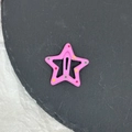 Barrette à cheveux étoile rose avec pois colorés posée sur un socle en pierre foncée - Rose