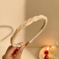 Detail van een crème gevlochten haarband met fijne parels bij warm licht - Off-wit