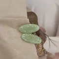 Close-up of mint green oval resin hair clips with golden foil flakes on kraft paper - Green