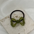 Detalle de coletero con lazo de resina verde oliva y goma elástica sobre piedra blanca - Verde
