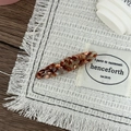 Détail macro d'une barrette en acétate écaille d'ambre sur lin et fond en bois - Motif Vert Brun