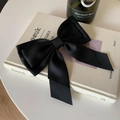 Primer plano de un elegante lazo de pelo en satén negro con cintas sobre un libro decorado - Negro