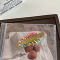 Dettaglio del fermaglio per capelli in lana intrecciata arcobaleno con base dorata - Giallo