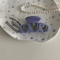 Detail der fliederfarbenen Acetat-Haarklammer mit hohlem Herzdesign auf Keramikteller - Blau