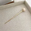 Detail of minimalist gold hair stick with cream ball bead on a textured beige tray - Off-white