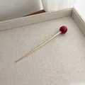 Detail of a minimalist gold metal hair pin with a large dark red bead on a linen tray - Red
