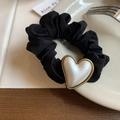 Detalle de un coletero de seda negra con colgante de corazón de perla dorada en plato cerámico - Corazón Blanco