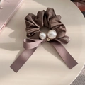 Elegante bruine satijnen scrunchie met parels en strikdecoratie op een tafel - Bruin