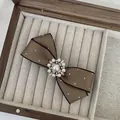Detalle de pasador para el pelo con lazo marrón, perlas y pedrería en caja de madera - Lazo de Cinta Marrón / Color Oscuro