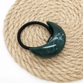 Detail view of dark green resin crescent hair tie with marble texture on straw mat - Green
