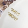 Coppia di fermagli dorati con design a triplo cuore vuoto su un piatto di ceramica - Oro