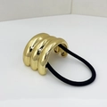 Detail of a minimalist gold metal cuff hair tie with a ribbed design and black elastic band - Gold