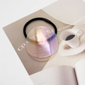 Dettaglio del ciondolo rotondo aurora su elastico per capelli nero con sfondo di rivista - Rosa Viola Olografico