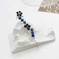 Dettaglio del fermaglio argentato con strass blu e fiore nero su supporto di pietra - Blu