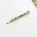 Close-up of golden bobby pin with ten multicolored round rhinestones on white base - Colorful