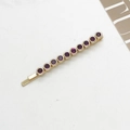 Dettaglio macro di un fermaglio per capelli dorato con dieci strass viola rotondi - Rosso