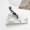 Détail d'une barrette argentée avec fleur noire, papillon et strass étincelants - Gris