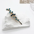 Detailed close-up of golden floral hair clip with blue rhinestones on a white pedestal - Sky Blue