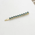 Dettaglio di un fermaglio dorato con dieci strass blu scuro su uno sfondo grigio - Blu