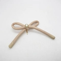 Detailed view of pink handmade bow hair clip featuring a central pearl and gold base - Beige
