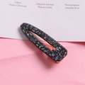 Close-up of marble pattern hair clip with gold metal base on a pink textured background - Waterdrop-Black