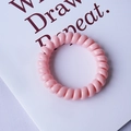 Pink spiral telephone cord hair tie in a macaron shade on a minimalist white card - Pink