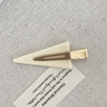 Triangle cream resin seamless hair clip with golden metal base on beige fabric background - Cream