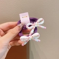 Set of two purple elastic hair ties featuring white star-print resin bows on card - Purple