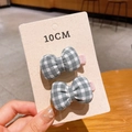 Close-up of grey plaid bow hair clips set on display card held by hand in warm lighting - Grey Plaid