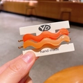 Set of two wavy orange acetate hair clips with gold metal base on display card - Orange Series