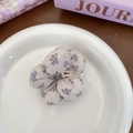 Chouchou en tissu à fleurs crème avec motifs violets posé sur une assiette céramique - Fleur Violette