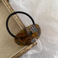 Detail of tortoise shell resin hair tie with amber and blue texture on wooden tray - Brown