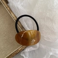 Amber tortoiseshell acetate oval hair tie with black elastic band on wooden tray - Coffee