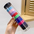 Vista dettagliata di elastici per capelli colorati in un contenitore cilindrico trasparente - Colori Misti