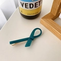 Elegant teal acetate ribbon bow hair clip with gold metal alligator base on white table - Lake Green