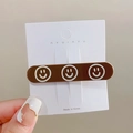 Brown rectangular hair clip featuring three white smiley faces on a brand display card - Brown Small Smile