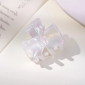 Close-up of bow-shaped acetate hair claw with iridescent white finish and gold lettering - Iridescent White