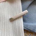 Dettaglio di un fermaglio per capelli beige rettangolare con una targhetta d'oro incisa - Bianco Latte