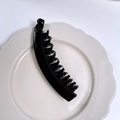 Glossy black banana hair clip with multi-tooth design on a white ceramic plate - Bright Black