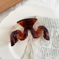 Elegant amber translucent wavy hair claw clip displayed on a decorative white porcelain plate - Tortoiseshell