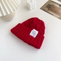 Thick red cable knit beanie with woven label detail on a minimalist white background - Red