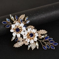 Detail van een gouden haarclip met smaragdgroene kristallen en witte bloembladen - Blauw