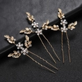 Detalle de tres horquillas doradas en forma de U con hojas, perlas y brillantes - Dorado