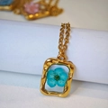 Dettaglio del ciondolo rettangolare vintage dorato martellato con un vero fiore blu - Stile Piccolo Fiore Blu