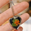 Macro view of heart-shaped stainless steel locket with real dried flowers on hand - Narcissus Heart Locket Necklace
