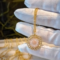 Close-up of golden openwork floral necklace held in gloved hand with nature background - Pink