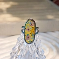 Makroaufnahme eines handgefertigten Harzrings mit Trockenblumen und Regenbogen-Edelstahl - Stil E Irisierende Basis