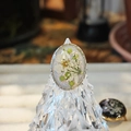 Detalle macro de anillo de resina artesanal con flores secas blancas y hojas verdes - Plata Púrpura