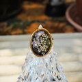 Detailed macro view of an oval resin ring featuring embedded dried flowers and pearls - Black Gold